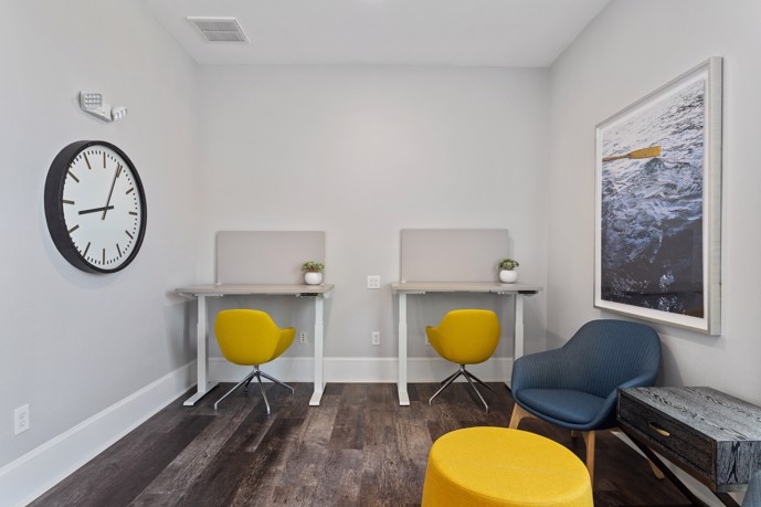 Common area work space with two small desks with yellow chairs and a large clock and modern artwork on the walls