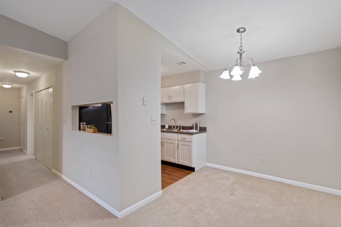 A cozy carpeted living and dining area adjacent to the kitchen within Spring Hill apartments, offering residents a comfortable space for gathering and dining.