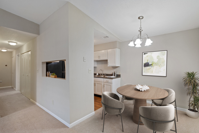 A cozy carpeted living and dining area adjacent to the kitchen within Spring Hill apartments, offering residents a comfortable space for gathering and dining.