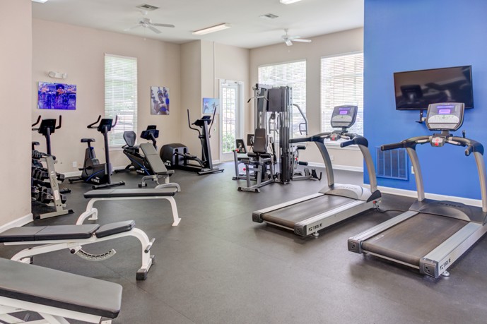 Apartment community fitness center with a variety of exercise equipment along the walls on the perimeter