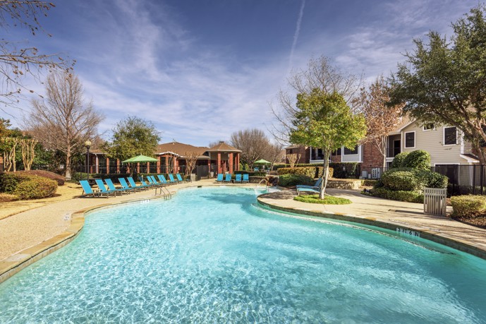 A large resort-style pool surrounded by lush vegetation and the apartments at The Delano at North Richland Hills.
