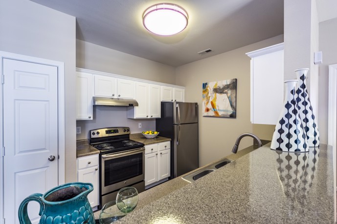 Beige apartment kitchen with a round ceiling lamp, granite countertops, white cabinets, and stainless steel appliances at Columns on Wetherington in Florence, KY