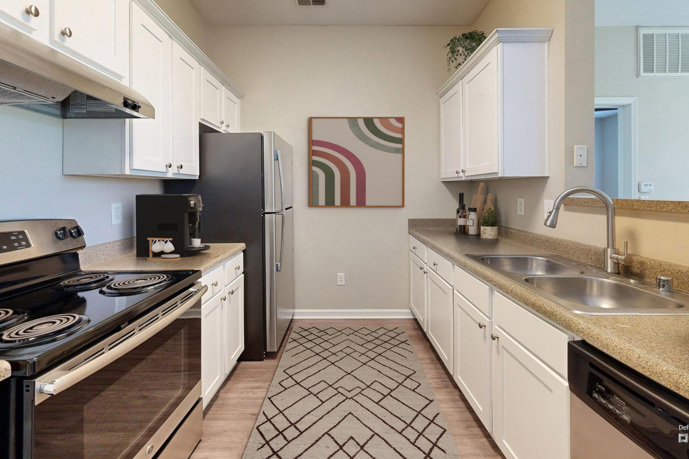 Beige apartment kitchen with a round ceiling lamp, granite countertops, white cabinets, and stainless steel appliances at Columns on Wetherington in Florence, KY