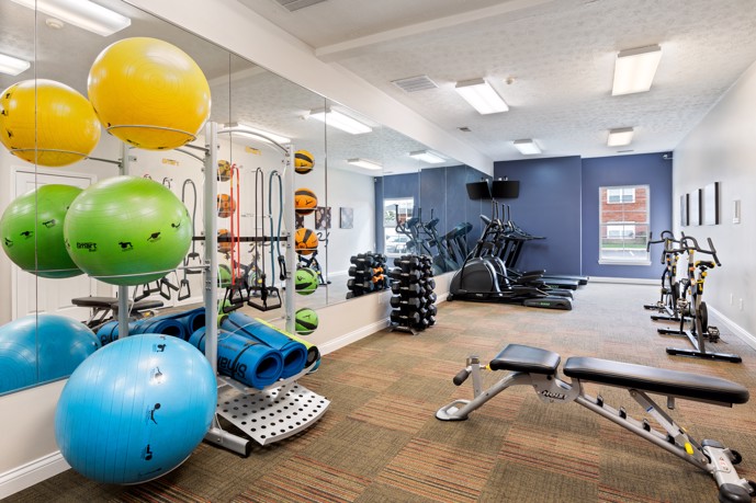 Fitness center featuring a wall of mirrors, various weights, cardio equipment, and gym balls.