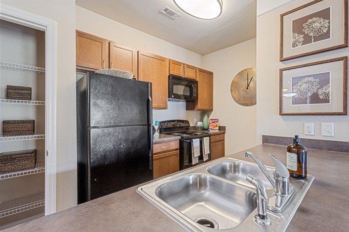 A kitchen with a sink, black refrigerator, and microwave at St James at Goose Creek.