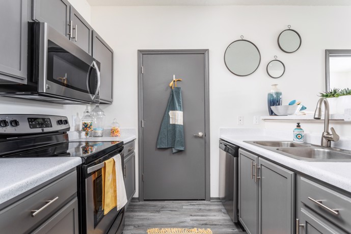Apartment kitchen with stainless steel appliances and grey painted cabinets facing a grey door