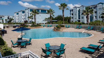 A serene and inviting poolside area at The Enclave at Tranquility Lake in Riverview, FL, featuring comfortable tables and chairs surrounded by lush greenery.