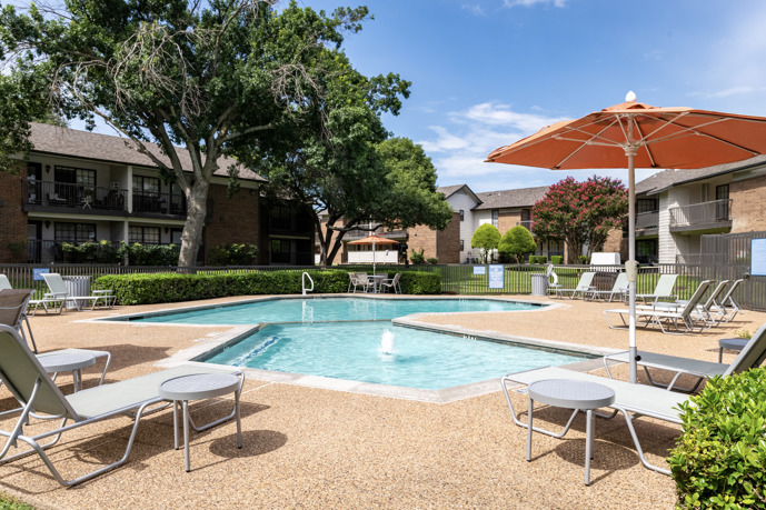 Outdoor pool surrounded by lounge chairs, tables, and umbrellas, set amidst stunning landscaping.