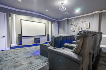 An elegant theater room features plush seating arranged in rows facing a large screen, with soft ambient lighting at The Enclave at Tranquility Lake.