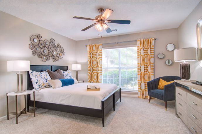 Bedroom adorned with a large window, ceiling fan, and plush carpeted flooring.