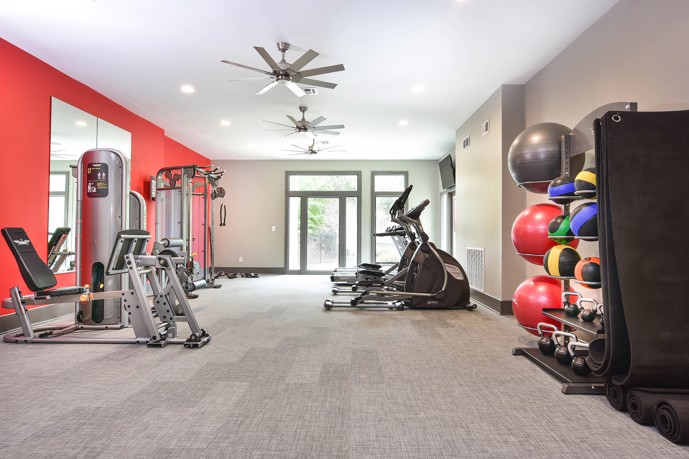 The fitness center at Westmont Commons equipped with a variety of gym equipment, featuring large windows, and accentuated by a vibrant red wall.