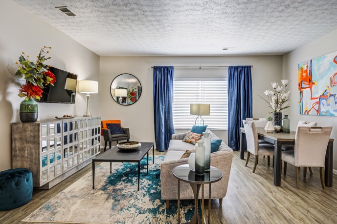 Enjoy a stylish living room at The Commons at Canal Winchester, featuring wood-style flooring, a comfortable grey two-seater couch, a large armoire, and a convenient dining table.