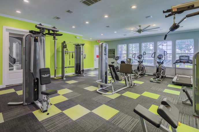Well-appointed fitness center offering weight and cardio equipment, ample natural light from large windows, and recessed lighting.