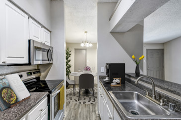 A galley kitchen with a view to the living area, stainless steel appliances, and granite countertops at Vue at Knoll Trail. 