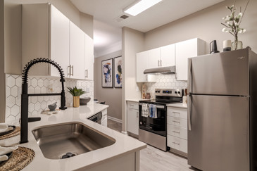A bright kitchen with stainless steel appliances, white cabinets, and a door to a laundry room at Residences on McGinnis Ferry. 