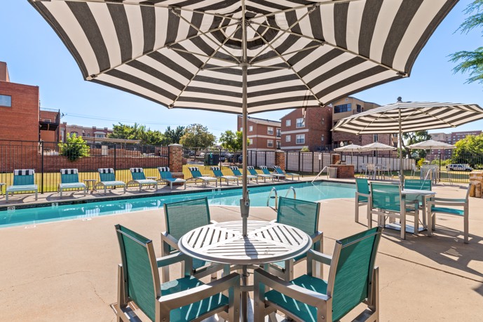 Long and narrow outdoor apartment swimming pool surrounded by blue pool chairs and black and white striped umbrellas 