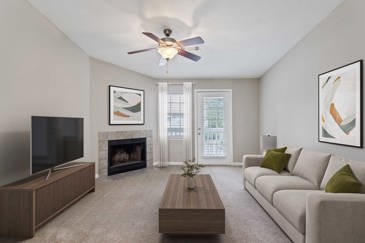 A carpeted living room with a corner fireplace for cold nights and a door leading to a balcony at the Villages at Spring Hill apartments.