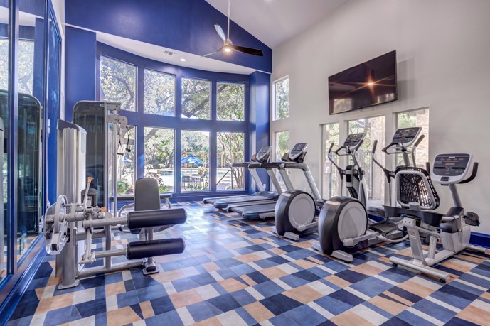 Community apartment fitness center with blue walls, natural light, TV, and exercise bikes for the residents