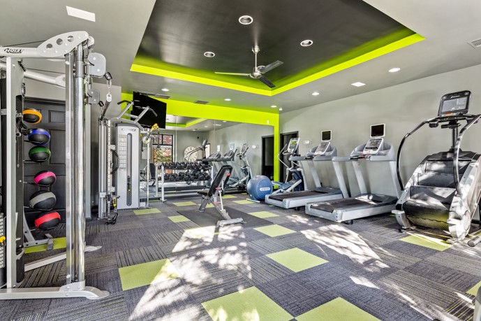 Grey and neon green apartment community fitness center with exercise equipment along one wall and exercise balls along the other