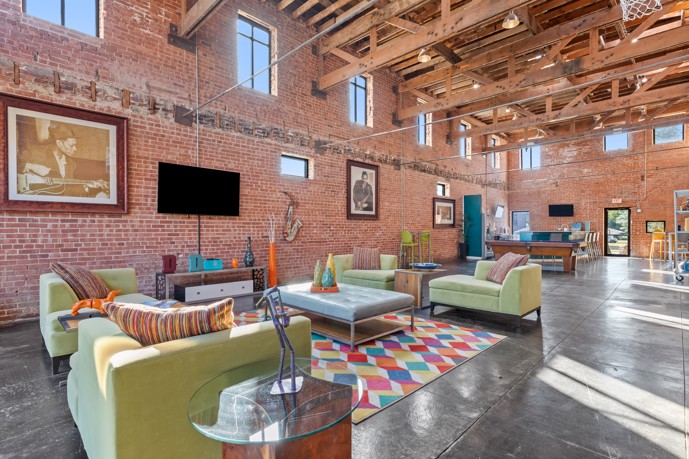 Large brick-walled apartment community clubhouse with grey concrete floors, exposed wooden ceiling beams, and a large seating area 