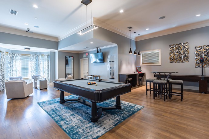 The clubhouse at Waterstone at Brier Creek in Raleigh, North Carolina, offers residents a comfortable gathering space complete with seating options, a pool table, and a shuffleboard for leisurely enjoyment.