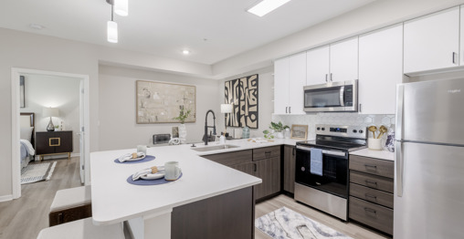 A modern kitchen with brown wood-style cabinets, quartz countertops, and a dining area adjoining it at a Columbus, OH apartment. 