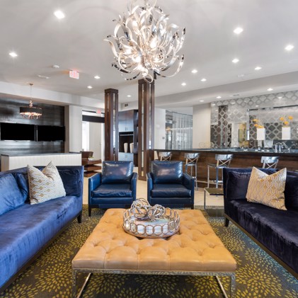Luxurious clubhouse at VV&M apartments with blue couches, kitchen bar, and chandeliers for residents to relax and socialize.