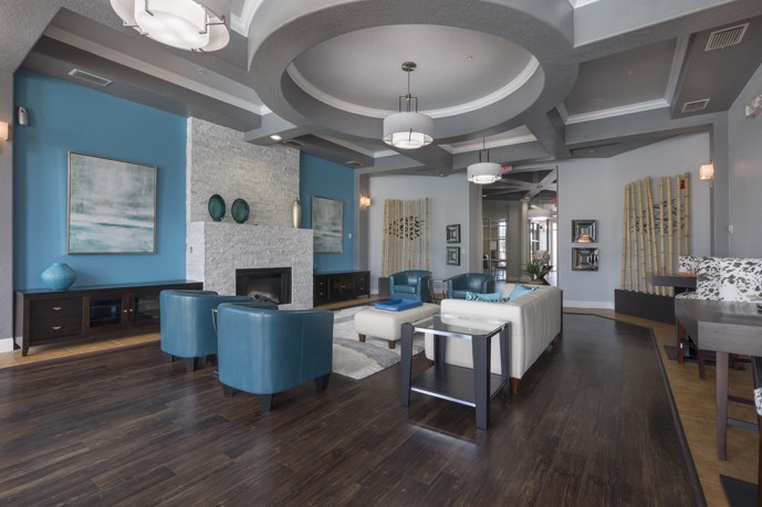 The inviting clubhouse at The Enclave at Tranquility Lake apartment complex, characterized by lofty ceilings, a cozy fireplace, and a table and chairs, providing residents with a stylish and comfortable communal area.