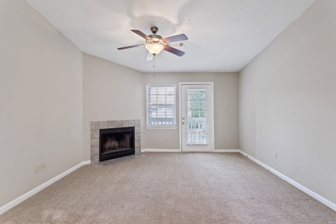 A warm and inviting carpeted living room within Spring Hill apartments, featuring a fireplace and windows that welcome natural light, creating a cozy atmosphere for residents to unwind.