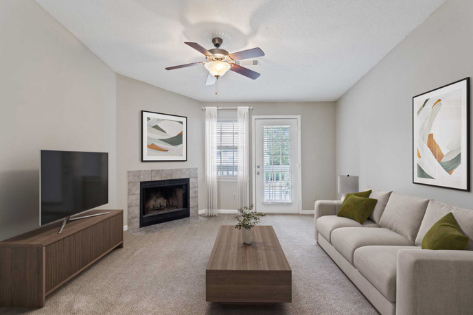 A warm and inviting carpeted living room within Spring Hill apartments, featuring a fireplace and windows that welcome natural light, creating a cozy atmosphere for residents to unwind.