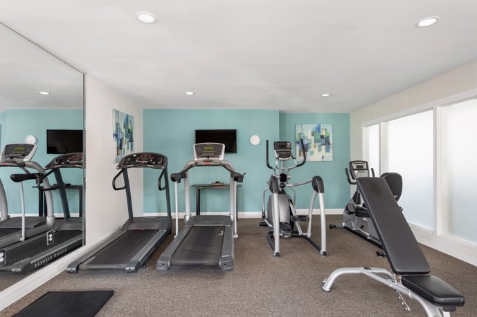 Small fitness center with a teal wall and five pieces of exercise equipment at Brookside apartment homes