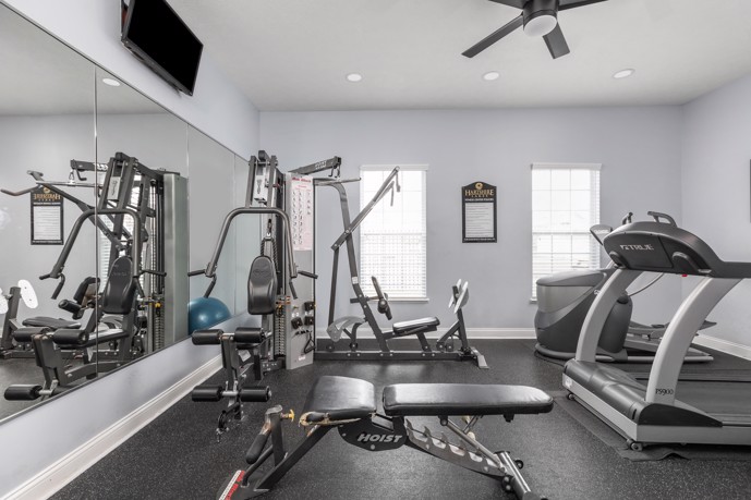 A fully-equipped fitness center with cardio and weight machines, mirrors, and a ceiling fan for comfort.