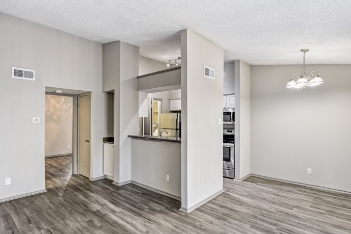A modern apartment at Vue at Knoll Trail featuring grey wood-style flooring, a chandelier in the dining area, and a fully-equipped kitchen