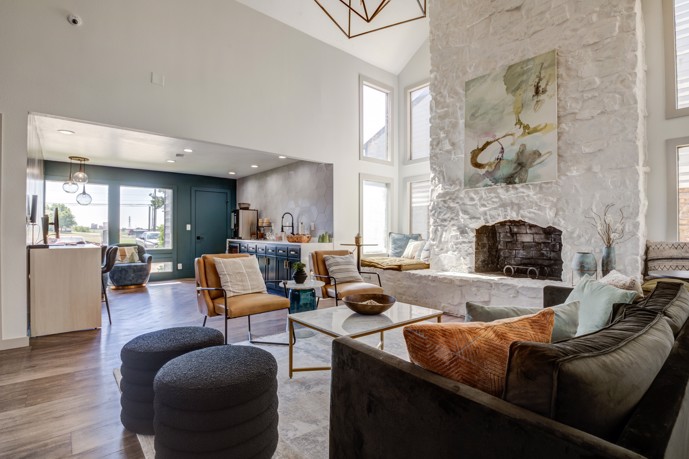 The contemporary and inviting clubhouse lounge at The Invitational, furnished with comfortable leather seating, a cozy fireplace, and soaring high ceilings, offering residents a stylish and relaxing space to unwind.