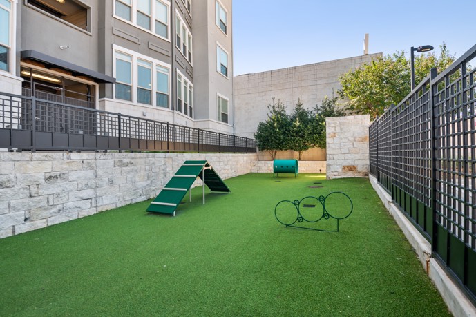 A fenced dog park located in front of the VV&M apartments in Dallas, Texas, featuring artificial grass and dog equipment, providing a safe and fun space for residents' furry friends to play and exercise.
