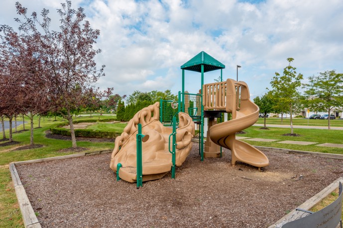 Outdoor playground adjacent to lush green grass, featuring a slide and climbing equipment, perfectly situated within the Hilliard Grand community.
