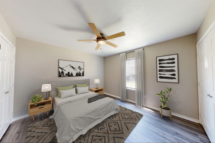 A modern bedroom at Windrush apartments, featuring grey wood-style flooring, a comfortable queen-sized bed, and a spacious walk-in closet.