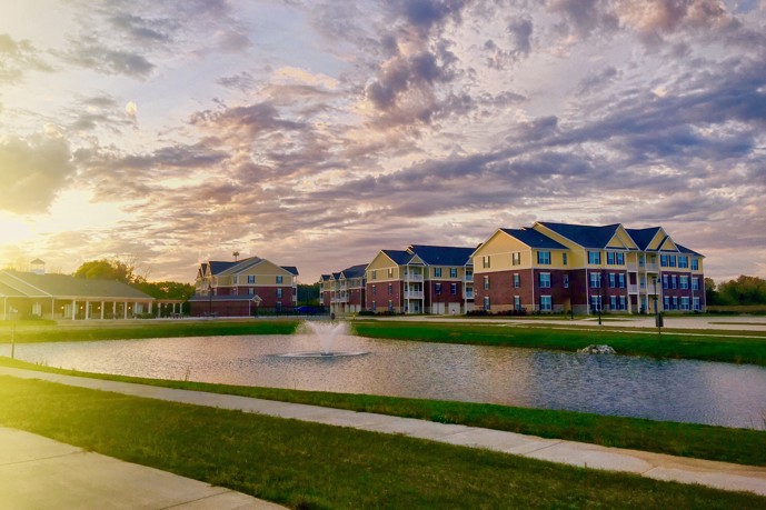 Exterior view of Double Creek Flats apartments in Plainfield, IN at sunset from across a pond with fountains
