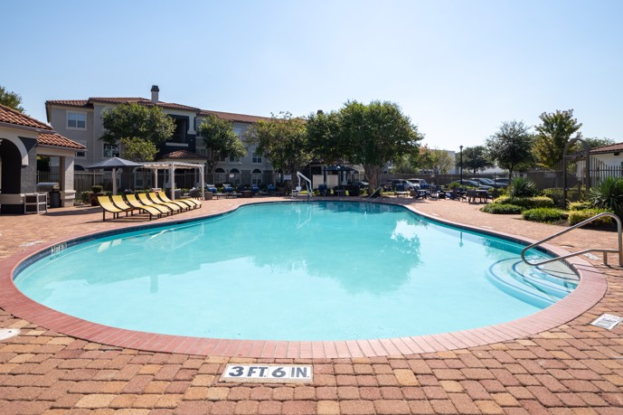 The resort-style pool with lounge chairs surrounded the apartments at Pointe at Vista Ridge in Lewisville, TX. 