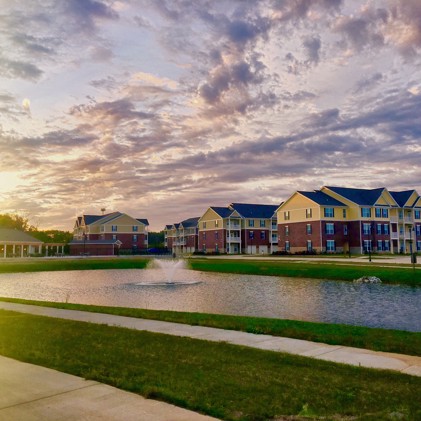 Exterior view of Double Creek Flats apartments at sunset from across a pond with fountains