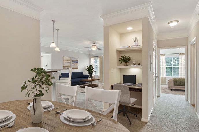 Long view of an apartment with neutral colored walls and wall-to-wall carpeting, window and open shelving in the middle of the room