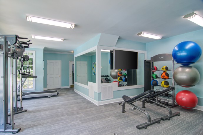 Fitness center furnished with exercise balls, a treadmill, weight machines, mirrors, and ample natural light through windows.
