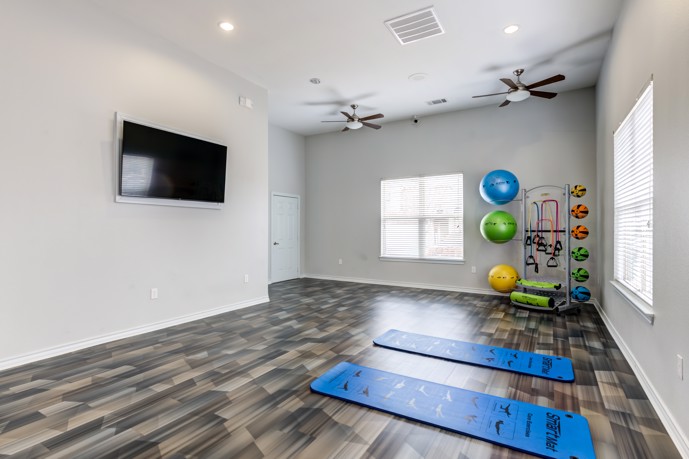 Residents fitness center with exercise balls, two mats on the hardwood floor, and a flat screen tv on the wall