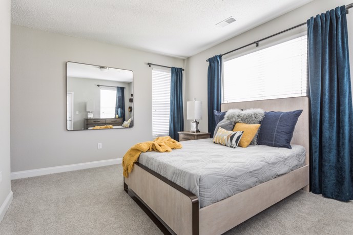 At The Village at Auburn, a comfortable bedroom, featuring a carpeted floor, a queen-sized bed, two windows, and a mirror.