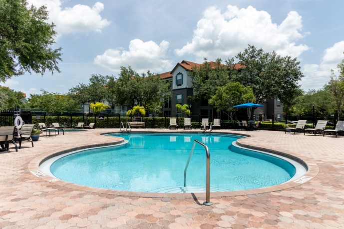 Swimming pool area including a spacious sundeck, inviting hot tub, numerous lounge chairs, and shaded umbrellas.