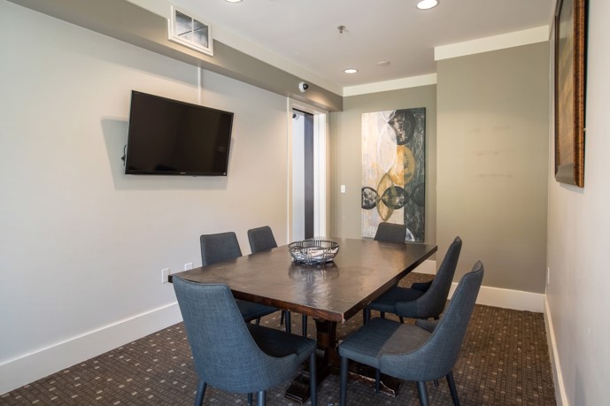 Resident-exclusive business enclave adorned with a sizable table, six chairs, a TV, and tasteful wall art, offering a productive sanctuary.