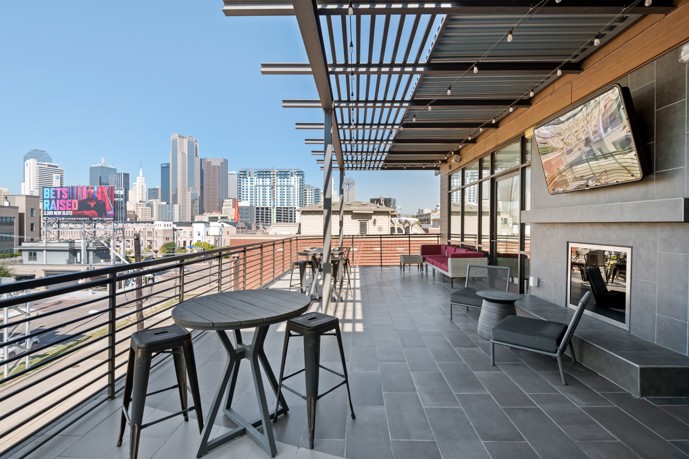 An outdoor rooftop sky deck with a pergola, seating, outdoor fireplace, modern tile, and city views