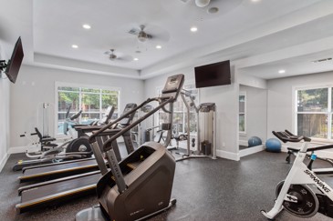 Fitness center at Carrington Place apartments with lots of windows, two flat screen TVs, and stationary exercise equipment