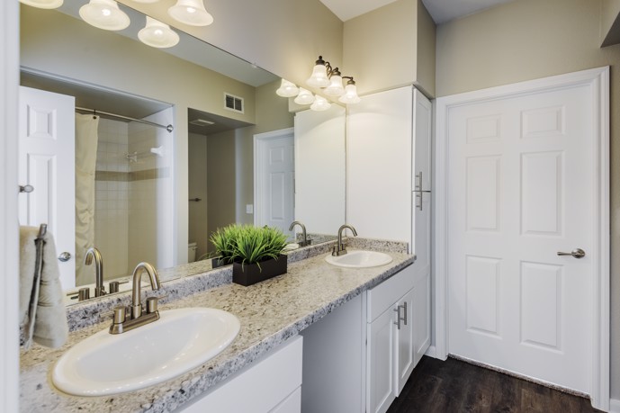 A bathroom with elegant granite counter tops and sleek white cabinets.