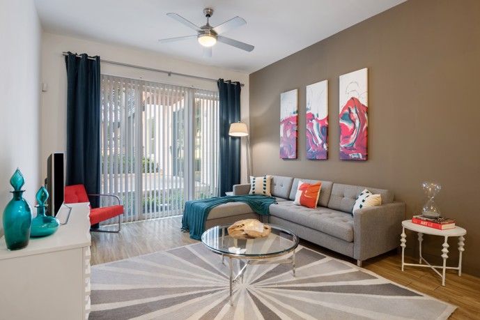 A cozy living room at VV&M apartments, featuring a grey sectional, wood-style flooring, and sliding doors leading to a patio, providing residents with a comfortable and inviting space.